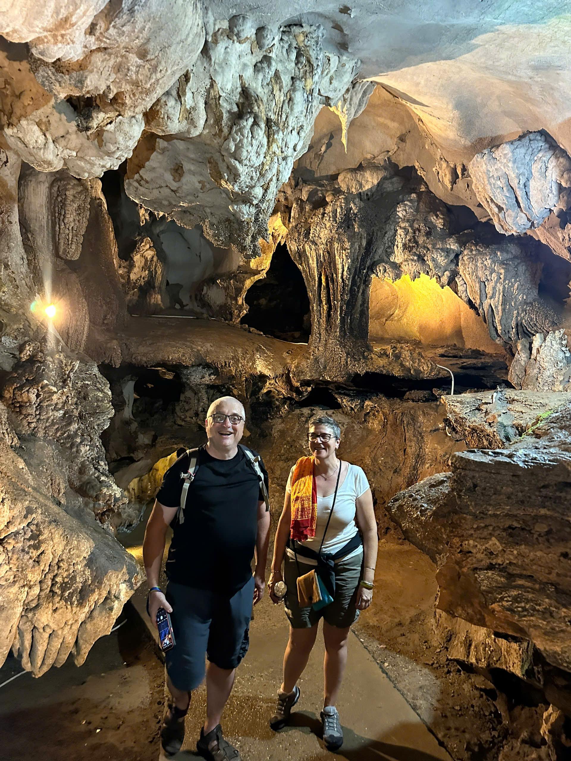 Two travellers with backpacks walking through a large cave chamber