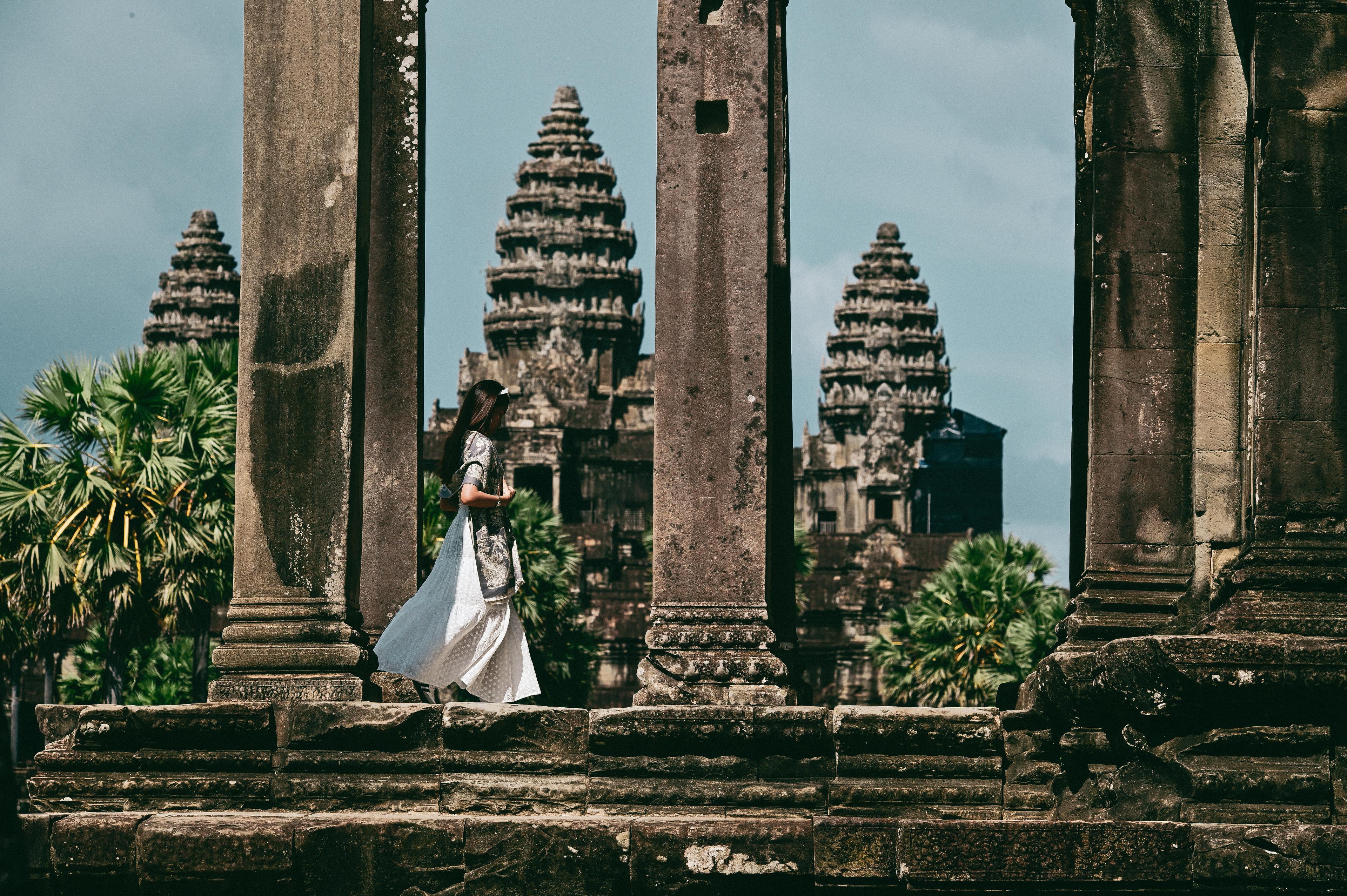 Una persona con un abito bianco cammina tra le colonne di pietra di Angkor Wat