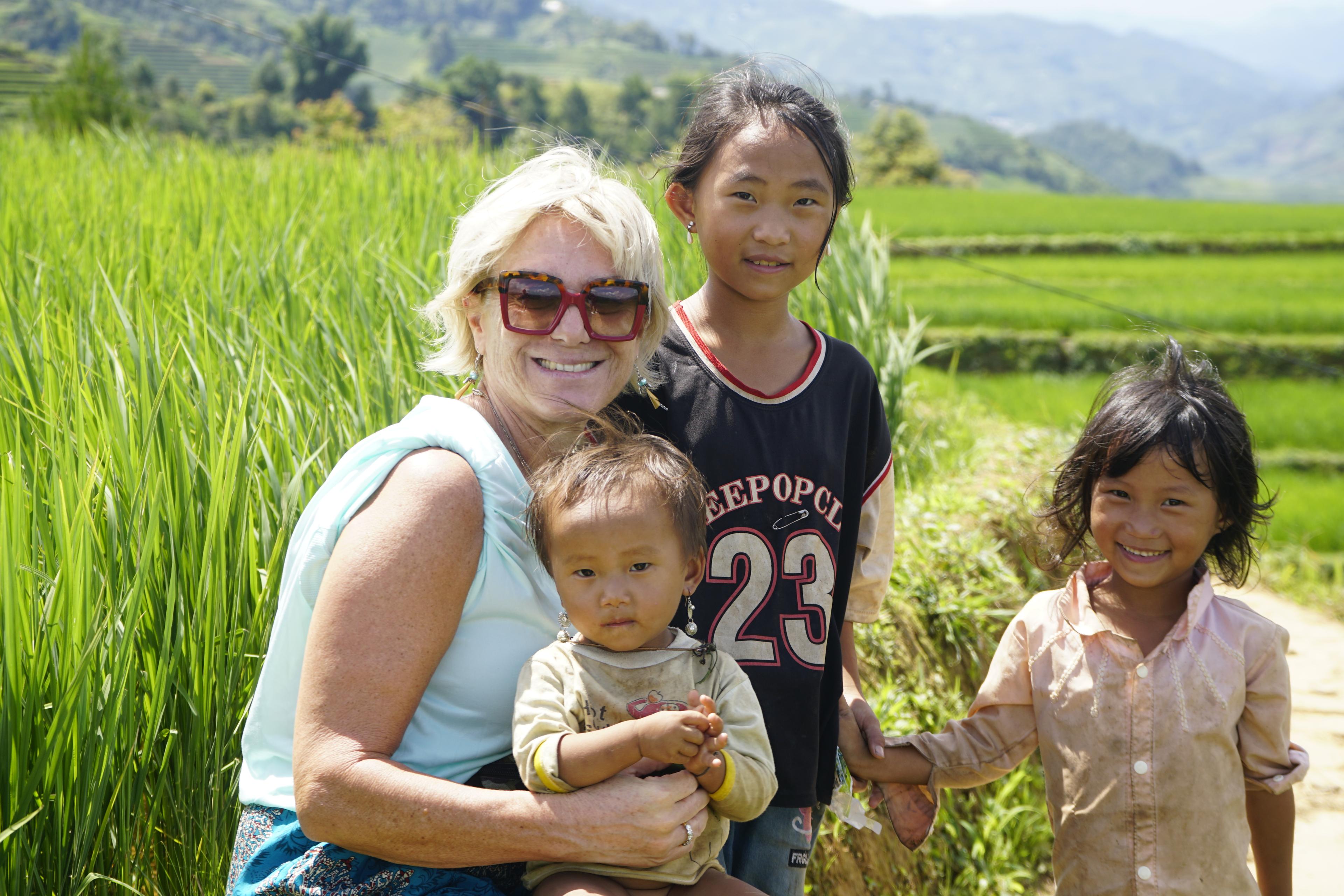 A traveller sitting with three local children beside a green rice terrace