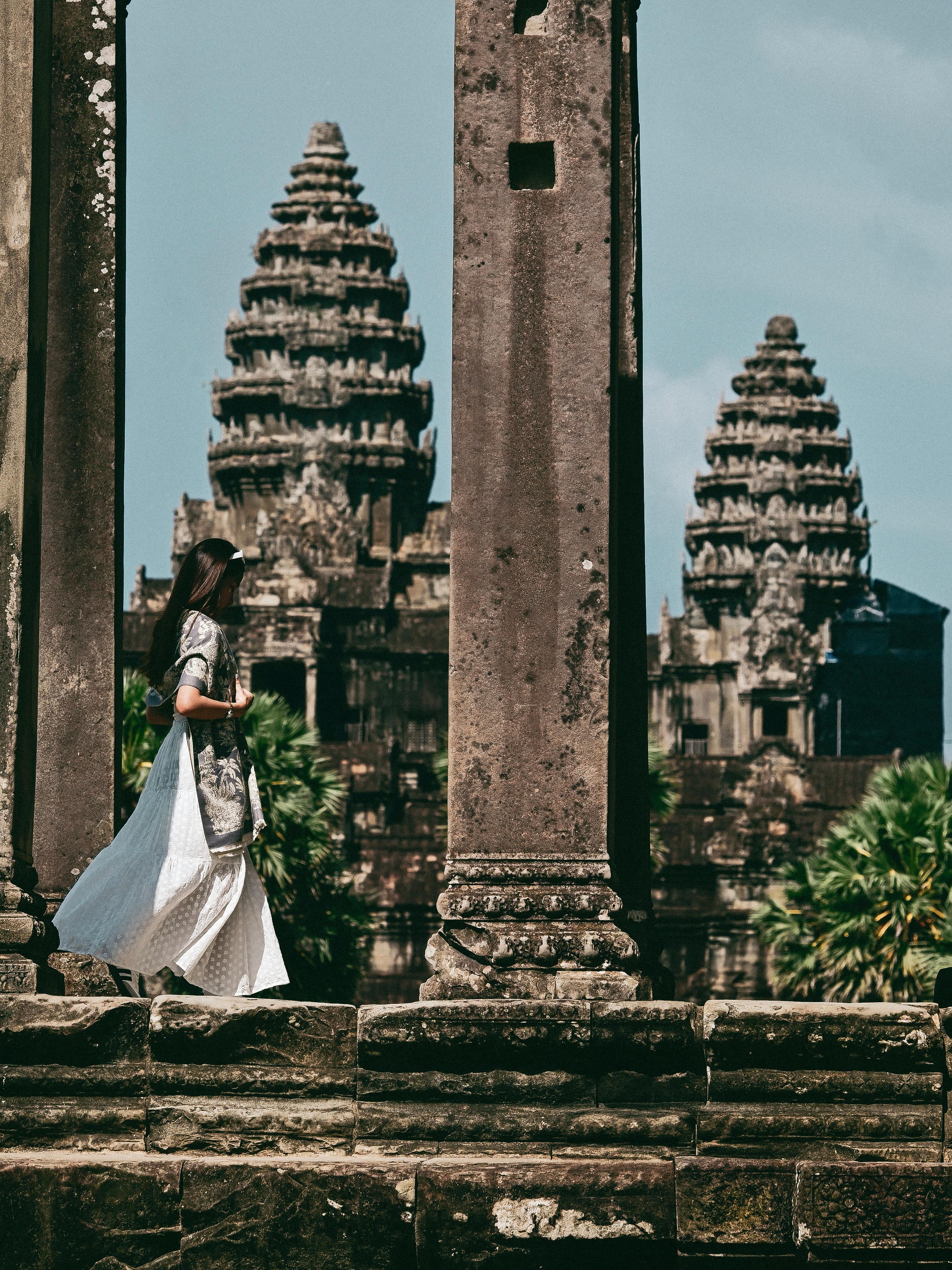 Woman walking between stone columns with the towers of Angkor Wat behind her