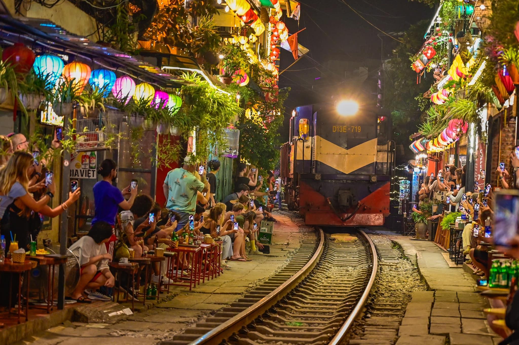 Un treno passa di notte tra i caffè illuminati dalle lanterne nella via del treno di Hanoi